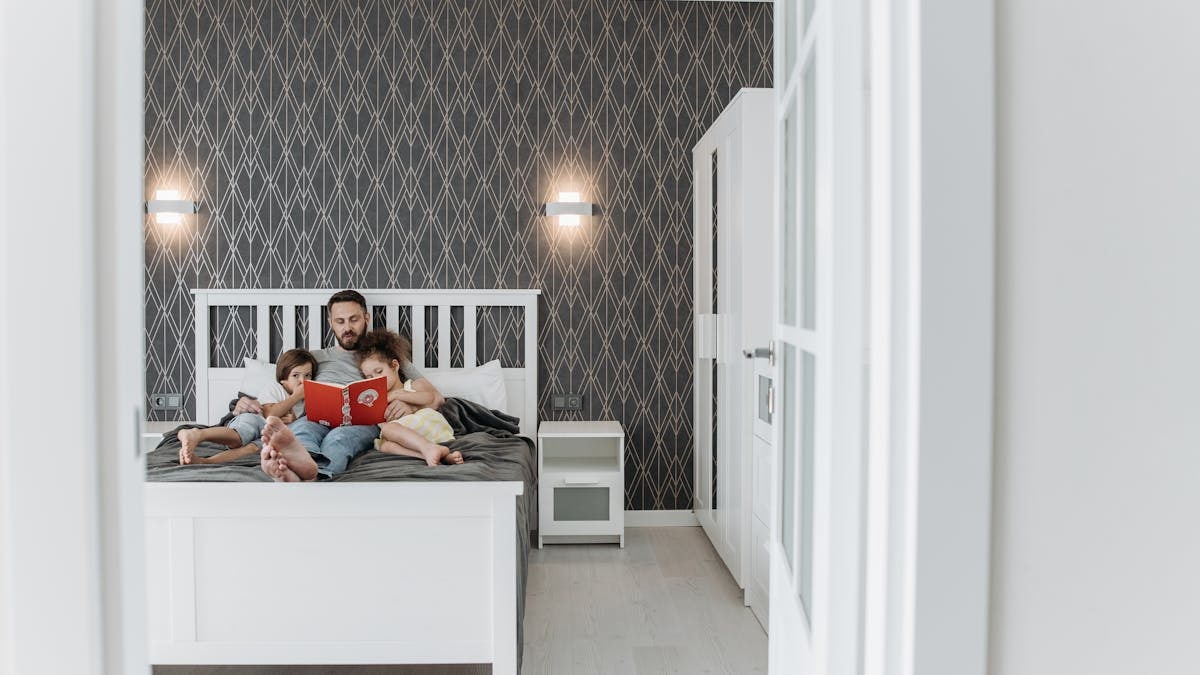 Father and children enjoy a bonding storytime in a cozy, modern bedroom setting.